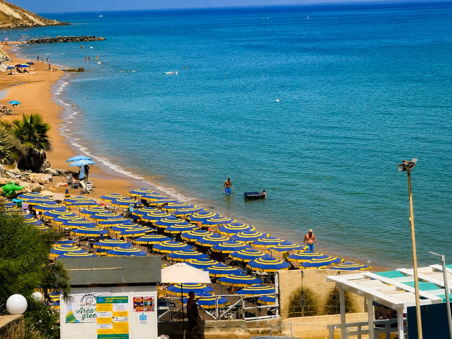 Il tratto di costa davanti al Santa Cristina Village, con spiaggia, mare e ombrelloni gialli e blu.