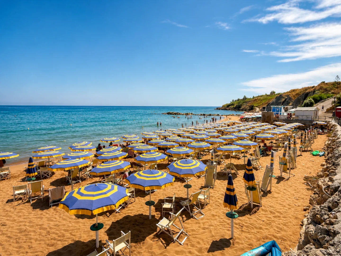 La spiaggia del Santa Cristina Village con il mare e gli ombrelloni celesti, gialli e blu.